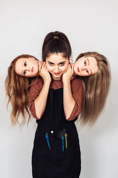 young girl hairdresser holds in hands two mannequin heads. Woman with three heads.