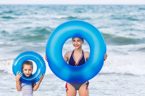 Szczęśliwy dziewcząt trzymać pływające nadmuchiwane kręgi na plaży morskiej. — Zdjęcie stockowe