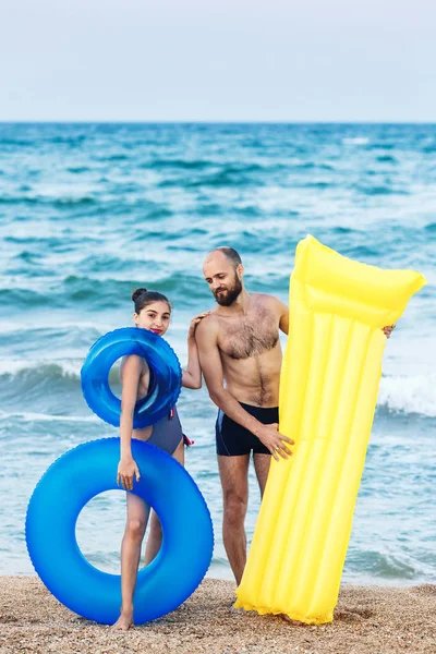 Radosny ojciec i córka stoją na plaży trzymając dmuchany materac i okrąg. — Zdjęcie stockowe