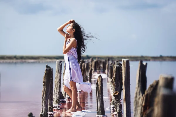 Bela menina em vestido branco longo posando no lago rosa salgado . — Fotografia de Stock