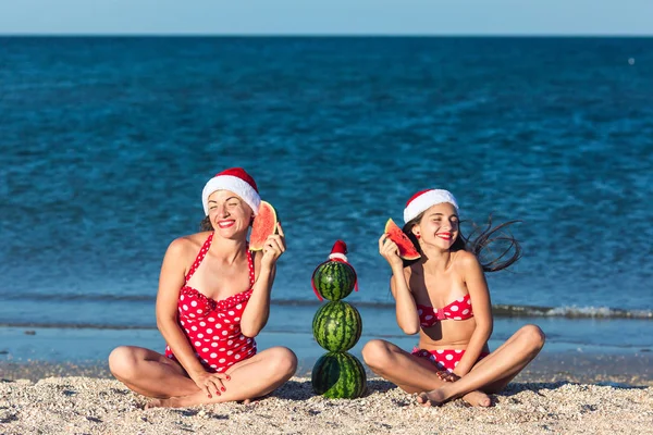 Matka i córka świętować lato Boże Narodzenie na plaży i jeść arbuz. Letni bałwan z arbuz. — Zdjęcie stockowe