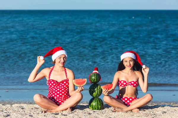 Mother and daughter celebrate summer Christmas on beach and eat watermelon. Summer snowman from watermelons.