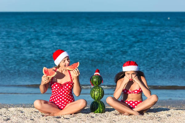 Mother and daughter celebrate summer Christmas on beach and eat watermelon. Summer snowman from watermelons.