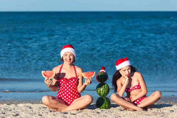 Mother and daughter celebrate summer Christmas on beach and eat watermelon. Summer snowman from watermelons.