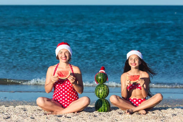 Mother and daughter celebrate summer Christmas on beach and eat watermelon. Summer snowman from watermelons.