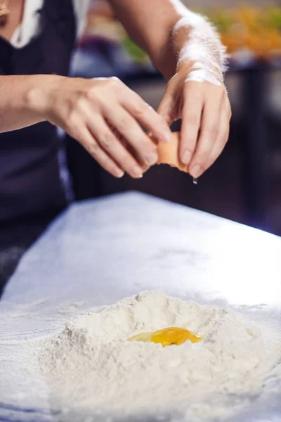 Baker breaks an egg into pile of flour. — Stock Photo, Image