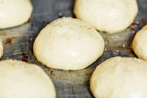 Close-up shots of raw round buns with sesame seeds lie on metal pan. — Stock Photo, Image