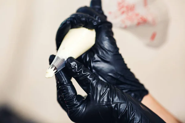 Primo piano dolcificante in guanti di gomma nera spreme crema dal sacchetto di pasticceria . — Foto Stock