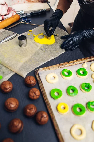 Pastry chef decorates raw profiteroles with green and yellow shortcrust pastry. — Stock Photo, Image