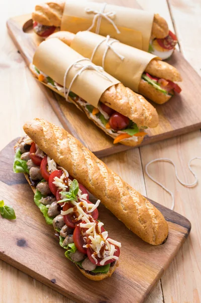 Tahta arka planda çeşitli dolguları olan taze denizaltı sandviçleri.