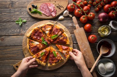 Tahta masada servis edilen salam dilimli taze pişmiş pizzanın en üst görüntüsü.