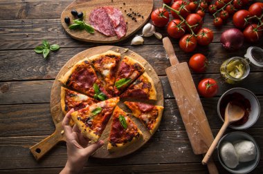 Tahta masada servis edilen salam dilimli taze pişmiş pizzanın en üst görüntüsü.