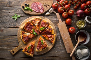 Tahta masada servis edilen salam dilimli taze pişmiş pizzanın en üst görüntüsü.