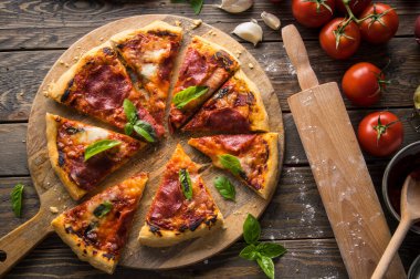 Tahta masada servis edilen salam dilimli taze pişmiş pizzanın en üst görüntüsü.