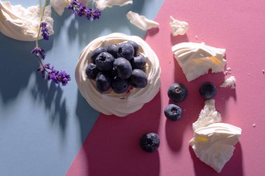 Pembe ve mavi arkaplanda taze böğürtlenli kremalı Pavlova pastası.