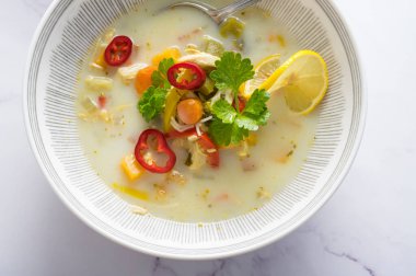 Sebzeli Rustik tavuk çorbası, erişte, limon dilimi, kereviz yaprakları ve mermer zemin üzerinde taze kırmızı biber.