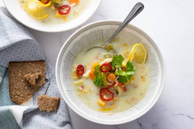 Sebzeli Rustik tavuk çorbası, erişte, limon dilimi, kereviz yaprakları ve mermer zemin üzerinde taze kırmızı biber.