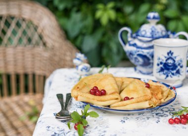 Kahvaltı krep, mavi ve beyaz renkli porselen, vintage şeker pot ve küçük heykel inek, kaşık, Bahçe, doğanın duvarına tabloda yapraklar ve arka plan üzerinde dokuma sandalye