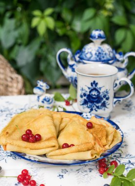 Kahvaltı krep, mavi ve beyaz renkli porselen, vintage şeker pot ve küçük heykel inek, kaşık, Bahçe, doğanın duvarına tabloda yapraklar ve arka plan üzerinde dokuma sandalye