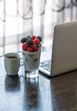 Kahvaltı chia tohum muhallebi bir bardak, fincan çay ev ofis, koyu ahşap masa, arka plan, iç olarak pencere üstünde laptop