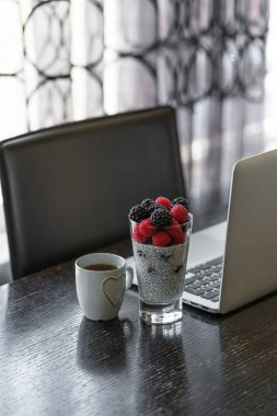 Kahvaltı chia tohum muhallebi bir bardak, fincan çay ev ofis, koyu ahşap masa, arka plan, iç olarak pencere üstünde laptop