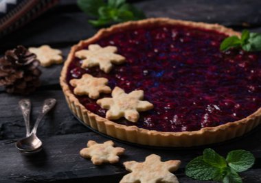 Noel tart, vişneli tart, rustik tarzda karanlık bir ahşap zemin üzerinde kar taneleri bisküvi, karanlık tarzı ile dekore edilmiş