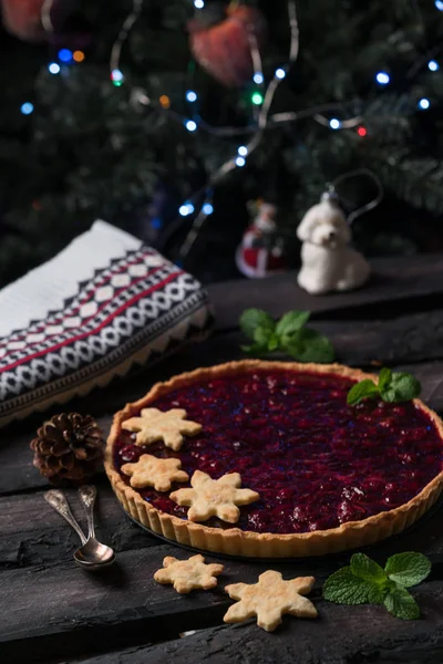 christmas tart, cherry tart on a dark wooden backdrop in rustic style, decorated with snowflakes biscuits, dark style