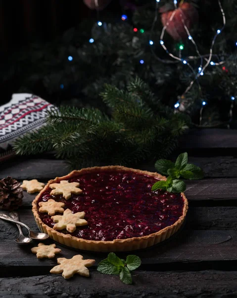 christmas tart, cherry tart on a dark wooden backdrop in rustic style, decorated with snowflakes biscuits, dark style