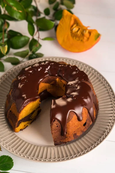 chocolate pumpkin cake, on white wooden backdrop, on grey rustic plate, chocolate glaze on top, pumpkin slices as decoration
