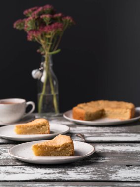 Ev yapımı limonlu kek rustik bir plaka üzerinde eski ahşap zemin, koyu arka plan, çay, buket çiçek, tatlı