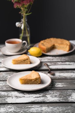 Ev yapımı limonlu kek rustik bir plaka üzerinde eski ahşap zemin, koyu arka plan, çay, buket çiçek, tatlı