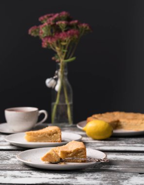 Ev yapımı limonlu kek rustik bir plaka üzerinde eski ahşap zemin, koyu arka plan, çay, buket çiçek, tatlı