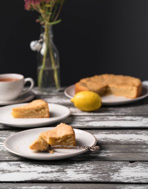 Ev yapımı limonlu kek rustik bir plaka üzerinde eski ahşap zemin, koyu arka plan, çay, buket çiçek, tatlı