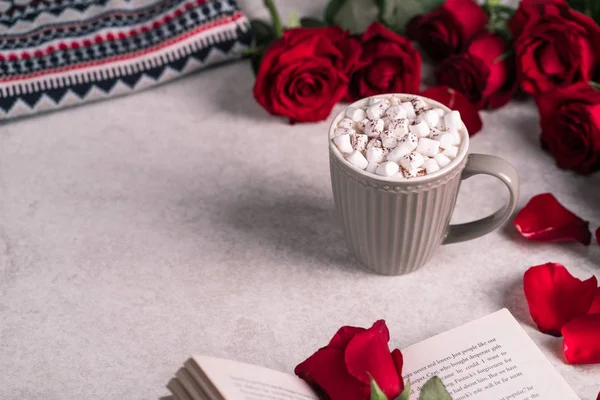 a drink topped with marshmallows in a grey cup, red roses on background, open food, festive season