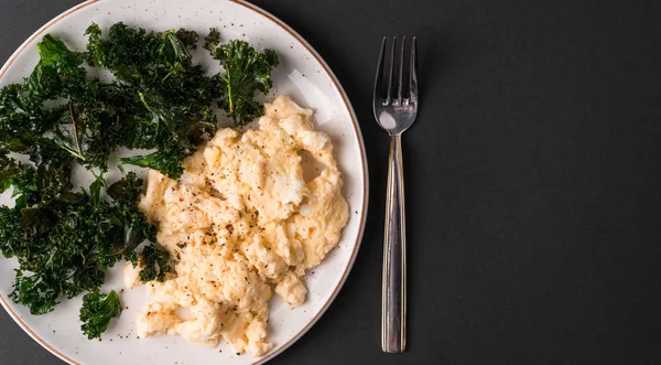 stock image kale chips and scrambled eggs breakfast on a dark background