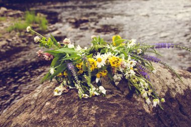 Nehir kıyısında büyük bir kayanın üzerinde yakınındaki nehrin kıyıya yakın yerde büyümek çiçek çelenk yatıyor.