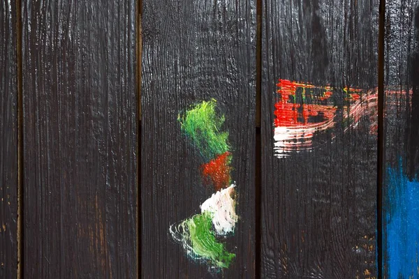 On a wooden background, which is painted with black paint painted with different colors of paint smears. Smears are done with a brush for drawing.
