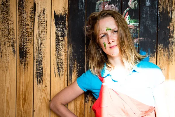 Güzel ve Genç kız boyalı duvar boyası arka plan üzerinde ayakta. Kızın yüzü bir yeşil boya ile lekeli - o bir fırça ile boyama, saçlarını rasped. Çok mutlu ve iyi bir ruh halinde olduğunu.