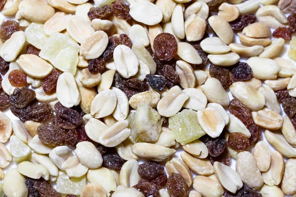 On a white isolated background lies a mixture of nuts and fruits. The mixture consists of peanuts, candied fruits, raisins and dried bananas.