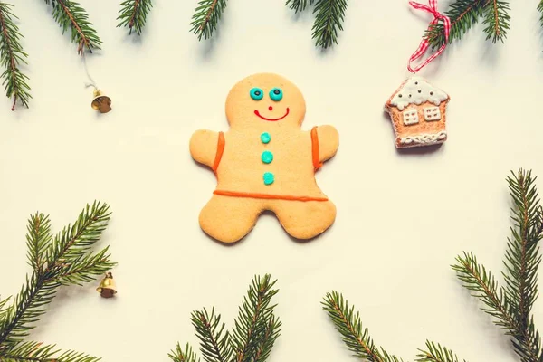 美味的烤姜饼人躺在白色的背景 它的周围是云杉树枝 上面挂着金色的小铃铛和姜饼屋 圣诞和新年的良好氛围 — 图库照片