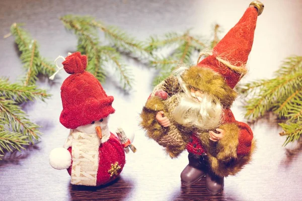 圣诞老人或圣诞老人站在一个新年雪人旁边的木背景与冷杉树枝 他们穿着节日的红色衣服 带着礼物给我们的家带来快乐 — 图库照片