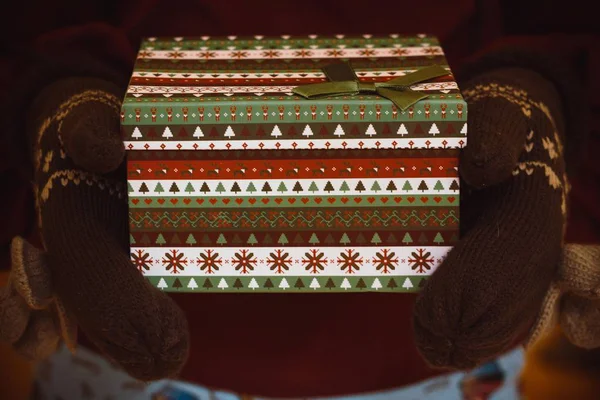 在温柔的手 穿着温暖的手套 拿着一个新年的盒子 其中期待已久的礼物 这个盒子装饰着美丽的圣诞图案 — 图库照片