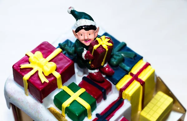 A toy in the form of a little man with a gift in his hands. Man sits on a set of gift boxes.