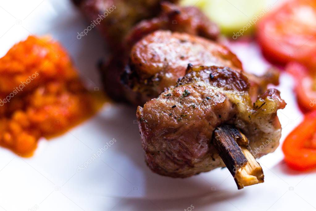 Very tasty cuts of meat are planted on a skewer and fried over an open fire. The meat lies on a white plate and will be served to the table with tomatoes and vegetable caviar. Very tasty food cooked in the open air.