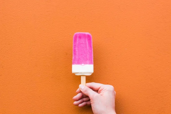 粉红色和白色色调的美味和冷冰淇淋在橙色的背景下 冰激凌昂贵的在温柔的女性手中 图库图片