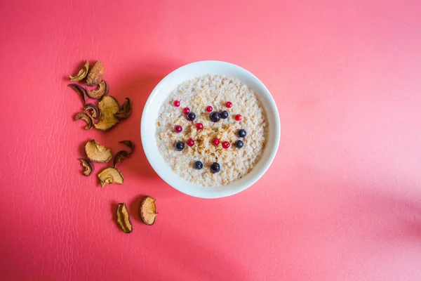 Süt ve çilek ile lezzetli karabuğday lapası. Tabağın yanında elma ve armuttan kurutulmuş meyveler vardır. Pembe tonnötr bir arka plan üzerinde bir tabak ve kurutulmuş meyve.