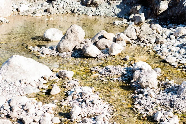 Clean river water flows between the stones. The sun\'s rays illuminate the stones and water.