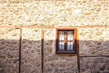 Taş bir evde parmaklıklar olan pencere. Ev kahverengi renkli taş bloklardan inşa edilmiştir. Eski evin penceresi metal bir ızgara ile kapatılmıştır..