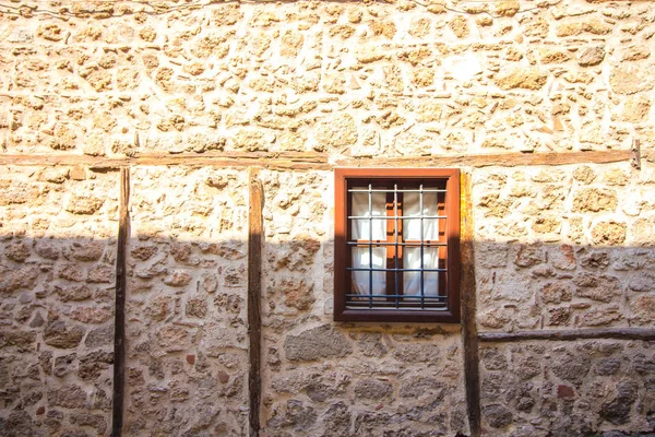Window with bars in a stone house. The house is built of brown colored stone blocks. The window of the old house is closed with a metal grill.