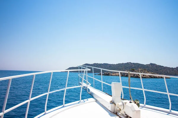 View of the mountains and the sea from the bow of the ship. Traveling by sea on a ship with beautiful scenery. The ship is white with a low railing. Sea water is clean and has a blue tint.